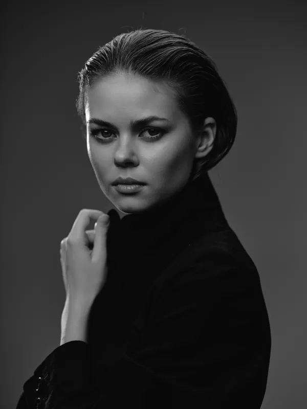 Black and white portrait of a serious woman in a black turtleneck with short hair and intense gaze.