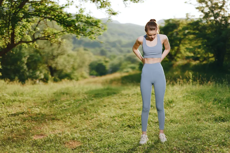 Young female athlete in a light blue sports outfit stretching in a lush green park, embodying fitness and wellness, surrounded by nature in a bright and refreshing setting