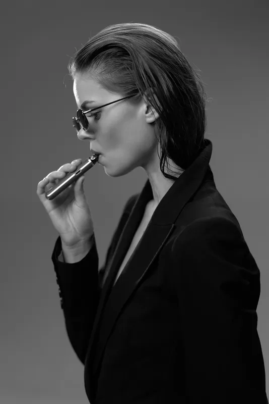 Black and white portrait of smoking woman with sunglasses in stylish jacket, contemplative mood, minimalistic background