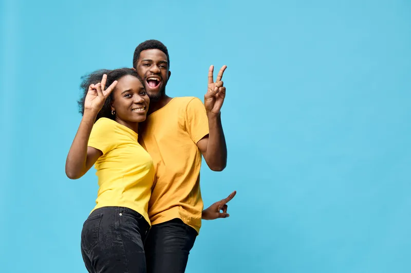 Couple in vibrant yellow outfits, joyfully posing against a light blue background, embodying happiness, youthfulness, and fun with playful gestures