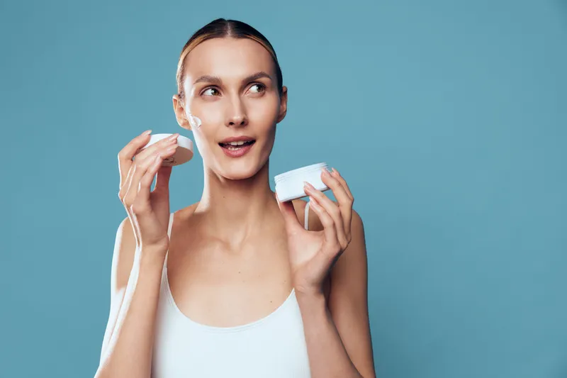 Woman skincare face beauty cleansing cotton hygiene wellness studio blue background, woman holding cotton pads to cleanse face, calm expression, soft light, minimal makeup, fresh skin care routine