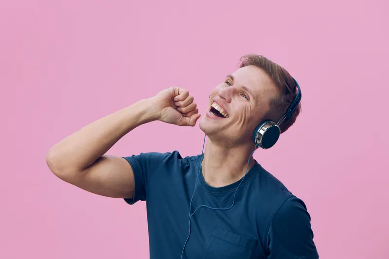 happy smiling young caucasian man with headphones enjoying music on pink background digital detox concept