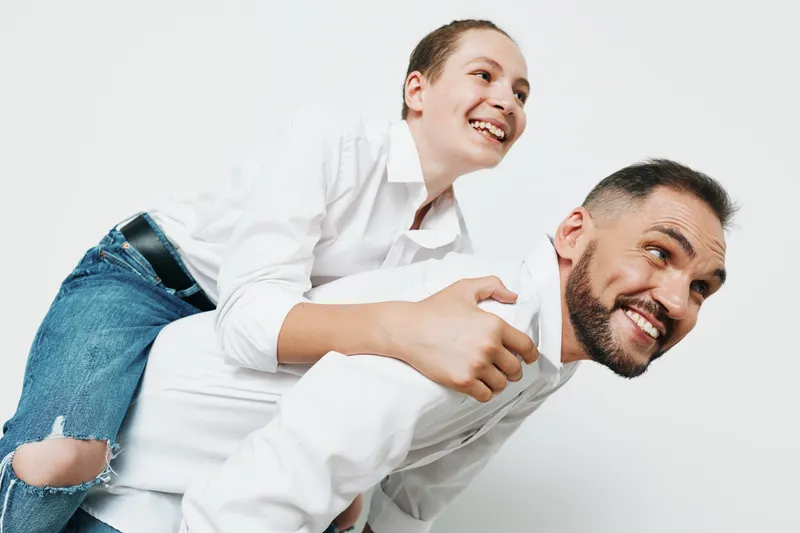 Professional man in business attire smiles while piggybacking a colleague, captured against an isolated white background. The scene conveys teamwork, confidence, and positive emotion for a dynamic,