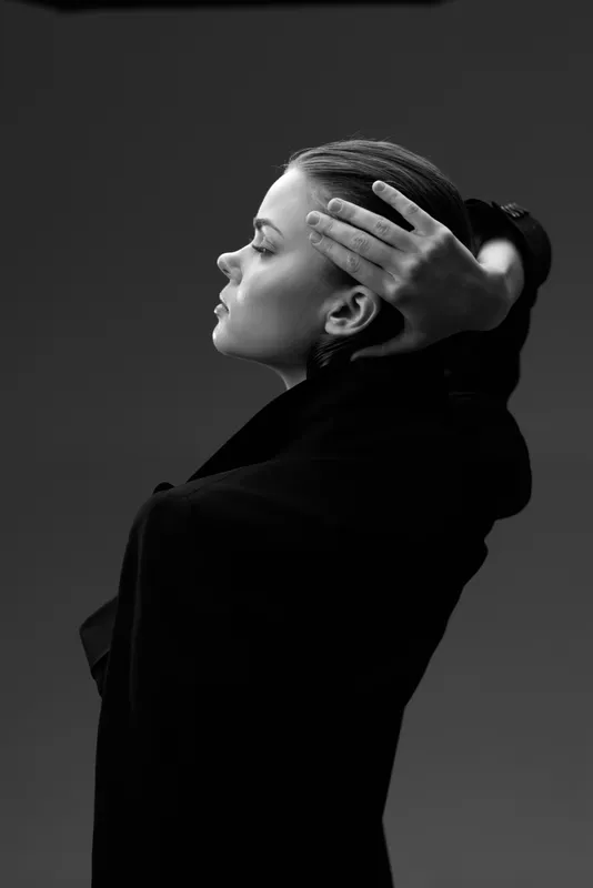Black and white portrait of a thoughtful woman with braided hair in stylish black clothing against dark background