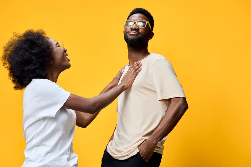 Joyful interaction between a young Black couple on a vibrant yellow background, showcasing playful emotions and casual style with a modern urban vibe