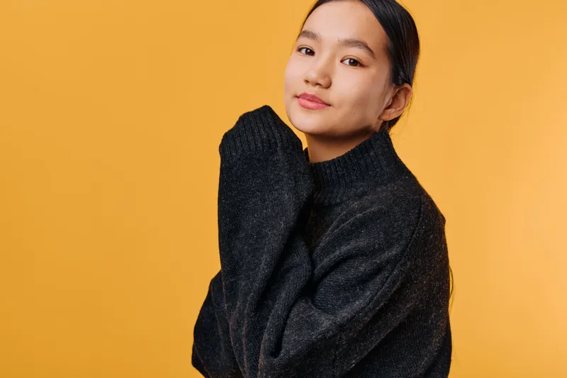 Young woman posing wearing black sweater on orange background looking confident with natural makeup and casual hairstyle in studio portrait with soft lighting mood