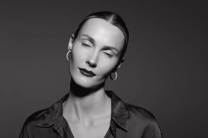 Portrait of a pale skinned European woman in black blouse with closed eyes and earrings. Studio black and white photography with soft lighting.