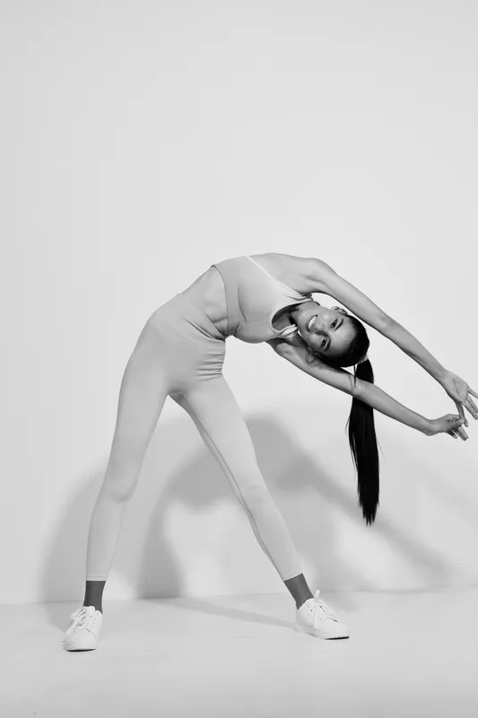 Sport fitness woman stretching in monochrome studio, wearing activewear and sneakers, showcasing flexibility and wellness in dynamic pose for healthy lifestyle.