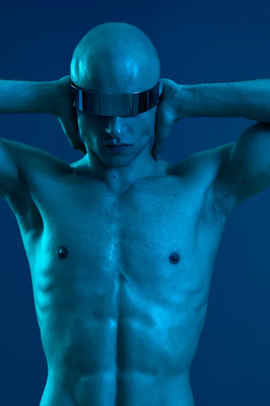 Striking man in futuristic sunglasses, showcasing a unique blue hue and captivating body art. The image captures a blend of modern aesthetics and bold expression.