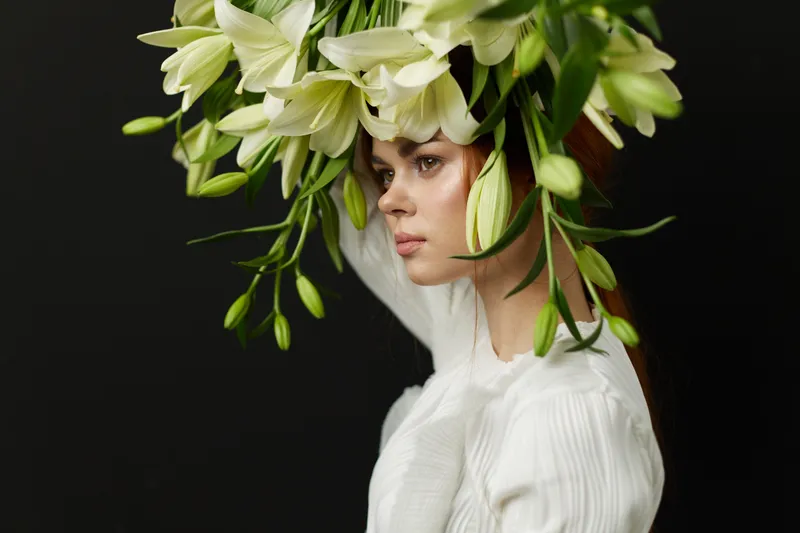 Beautiful woman with a floral crown made of white lilies against a dark background, conveying elegance and serenity in a fashion forward style