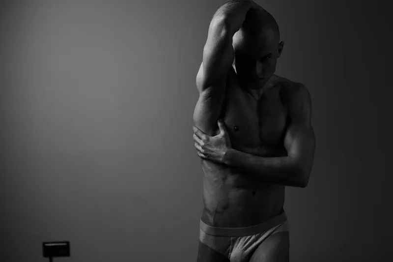 Black and white image of a strong man posing elegantly, showcasing his physique and expression in a dramatic and artistic manner.