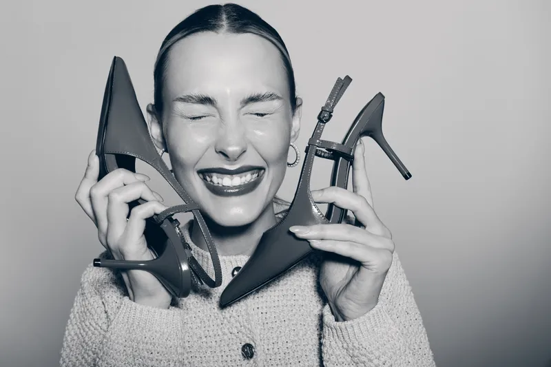 Happy caucasian woman with fair skin holds two high heel shoes near face with eyes closed. Concept of fashion, style, and footwear.