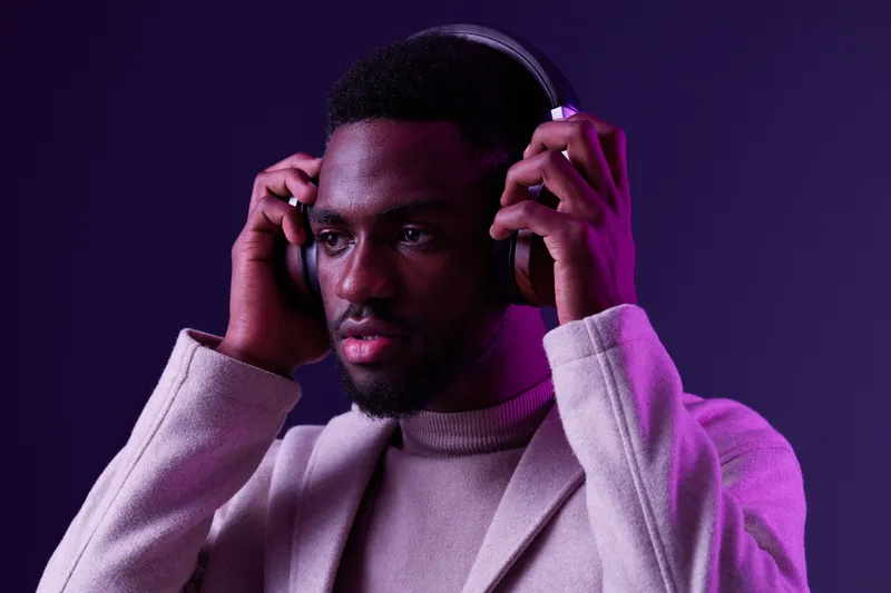 Young African man wearing stylish headphones, enjoying music, with a purple gradient background, conveying emotions of relaxation and focus