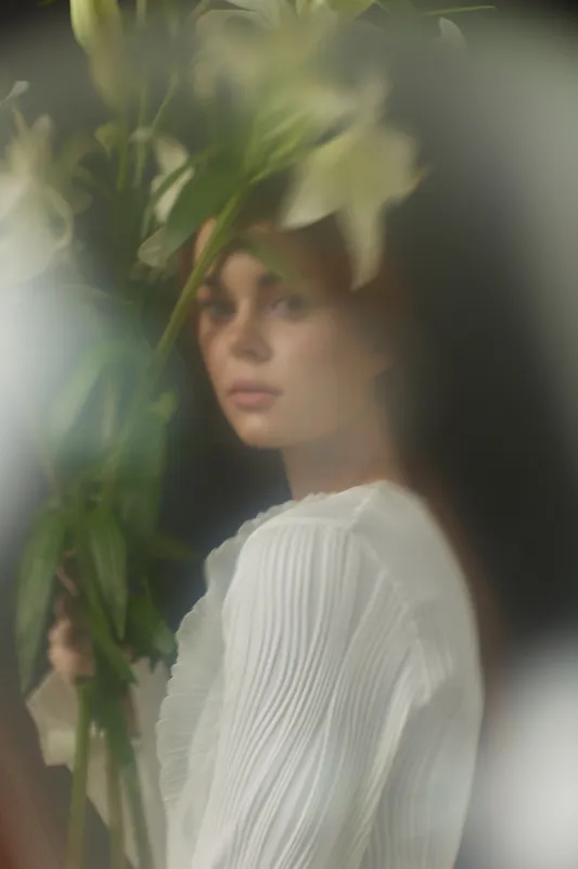 A young woman with flowing hair holds delicate flowers, embodying serenity and elegance against a soft, blurred background perfect for wellness concepts