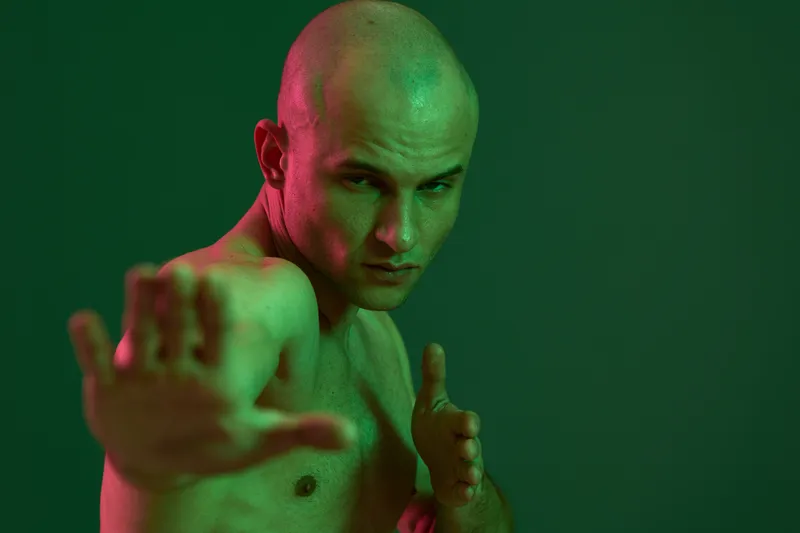 Athletic man posing dynamically in a dramatic green lighting, showcasing strength and determination with an intense expression, ideal for fitness concepts.