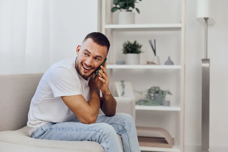 Smiling man engaged in heartfelt conversation, embodying emotional connection and vulnerability in a modern, cozy living space, capturing the essence of authentic masculinity.