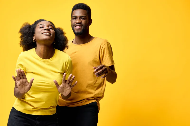 Joyful young Black couple dancing together in vibrant yellow clothing against a bright yellow background, expressing happiness and positivity