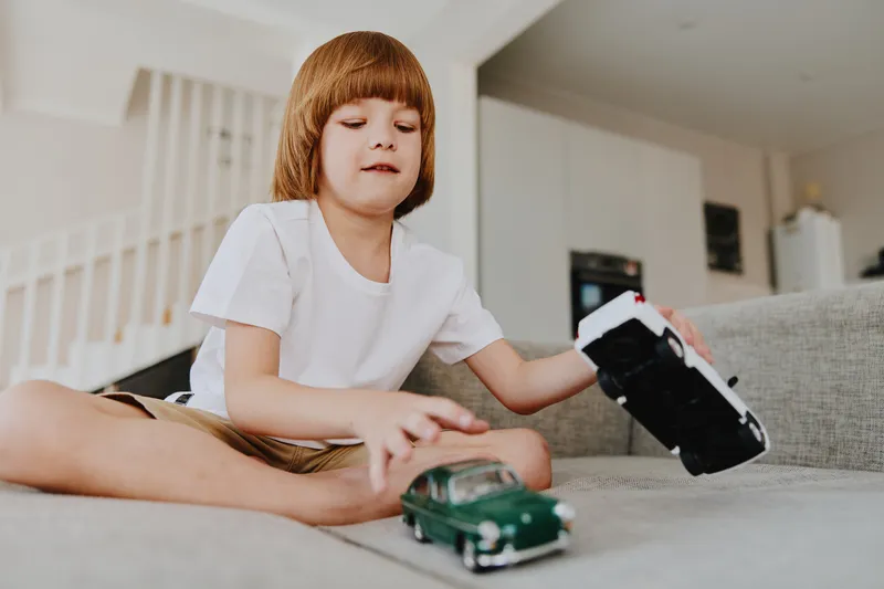 Happy boy playing with toy cars at home, smiling joyfully in a cozy living room filled with natural light.