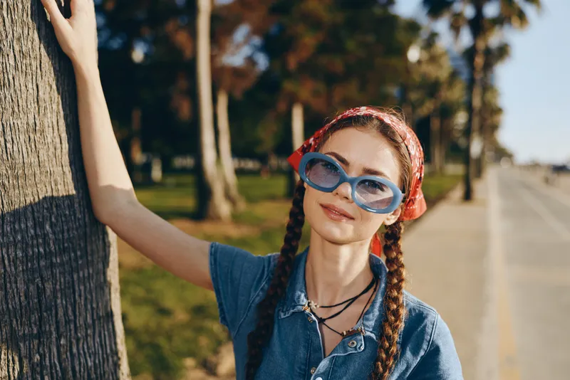 Lifestyle woman in modern boho-western denim street style wearing blue sunglasses and a red headband with braided hair, captured in warm film color outdoors.
