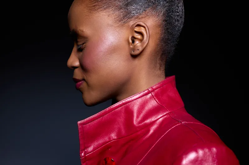 Profile of a dark skinned African woman with short hair wearing a red leather jacket against black background. Concept of fashion, beauty, confidence, and portrait photography.
