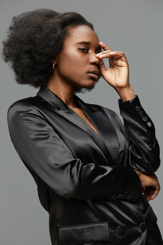 Stylish African woman in a black satin blazer with natural hair, conveying confidence against a neutral grey background, perfect for fashion and empowerment themes