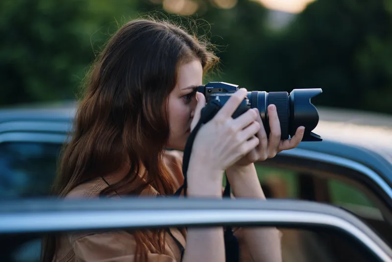Young woman photographing outdoors with a professional camera, capturing moments in nature, showcasing creativity and passion for photography.