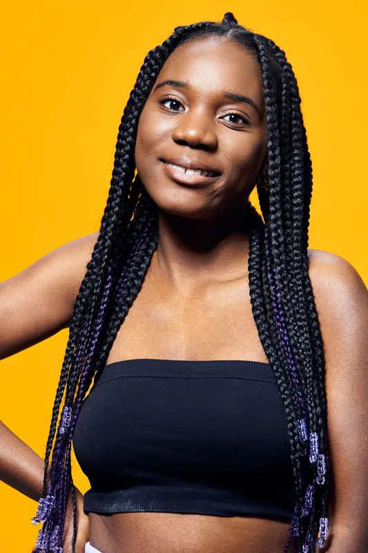 Young Black woman with braided hair smiling against a vibrant yellow background, showcasing her confidence and style through casual fashion