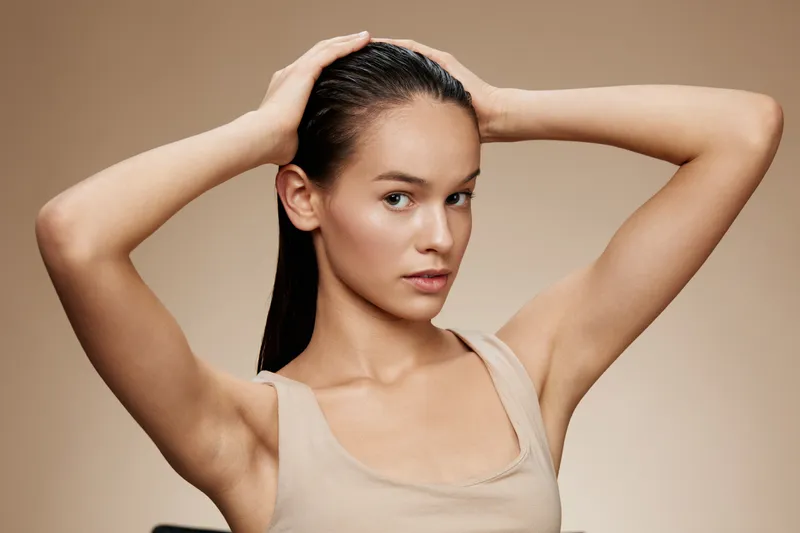 Young woman with long hair posing against a neutral background, showcasing healthy hair and natural beauty, highlighting self care and confidence