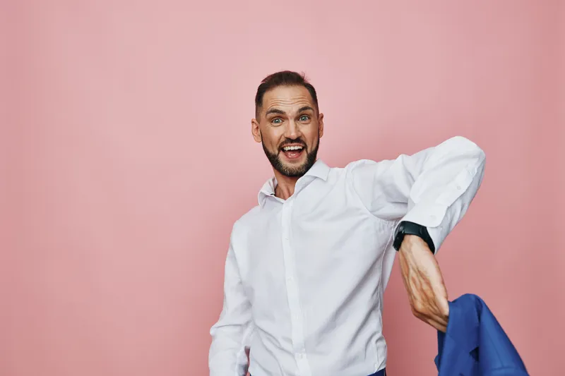 Theme: business, professional mood with an isolated pink background. A confident man in a white shirt shows emotion with a broad smile as he adjusts his jacket.