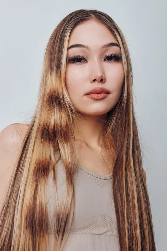 Young woman with long straight hair posing in neutral top against white background with natural makeup and calm confident expression for portrait photography.