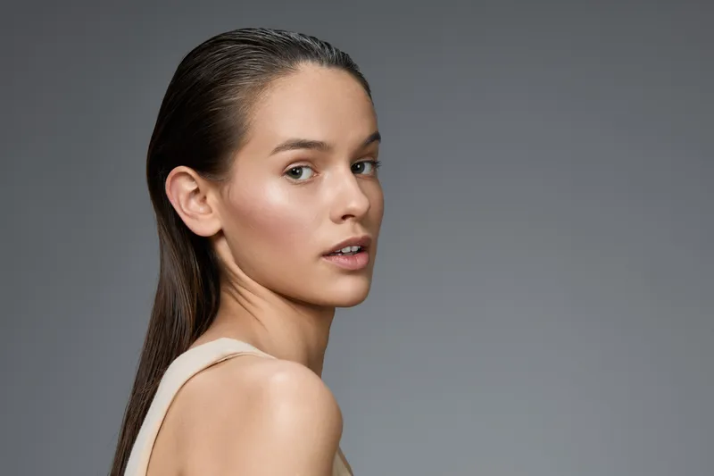 Portrait of a young model with long, wet hair, showcasing natural beauty and elegance against a minimalist gray background, perfect for beauty and skincare concepts