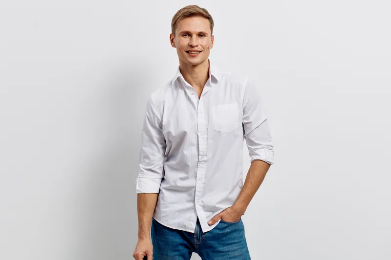 Smiling man in white casual shirt posing against plain white background, confident and friendly expression, casual clothing, studio portrait, lifestyle concept, young adult male.