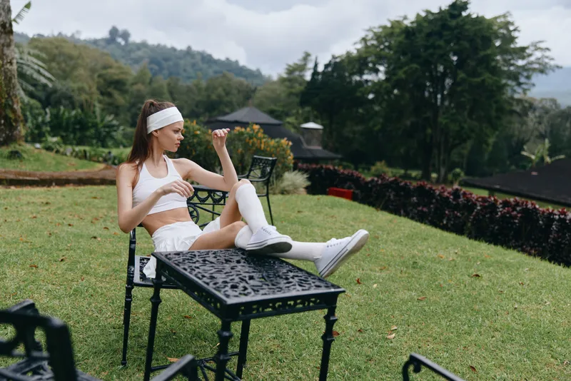 Young woman in athletic wear sitting outdoors, enjoying a moment of relaxation on a sunny day, conveying a sense of tranquility and freshness