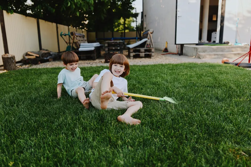 Happy children playing in the yard, enjoying a sunny day outdoors with laughter and joy. Bright green grass and playful atmosphere create a vibrant scene.