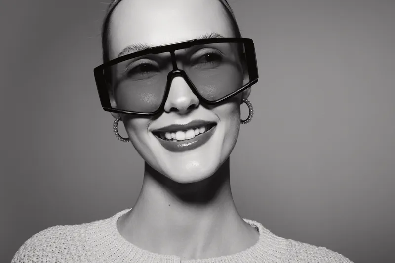 Smiling caucasian woman with pale skin wearing large sunglasses and hoop earrings isolated on grey background. Concept of fashion, style, beauty, and modern accessories.