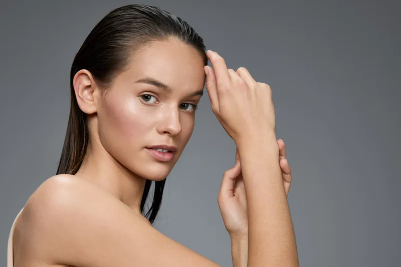 A beautiful young model with wet hair gently touching her face, showcasing a natural and serene expression against a soft gray background