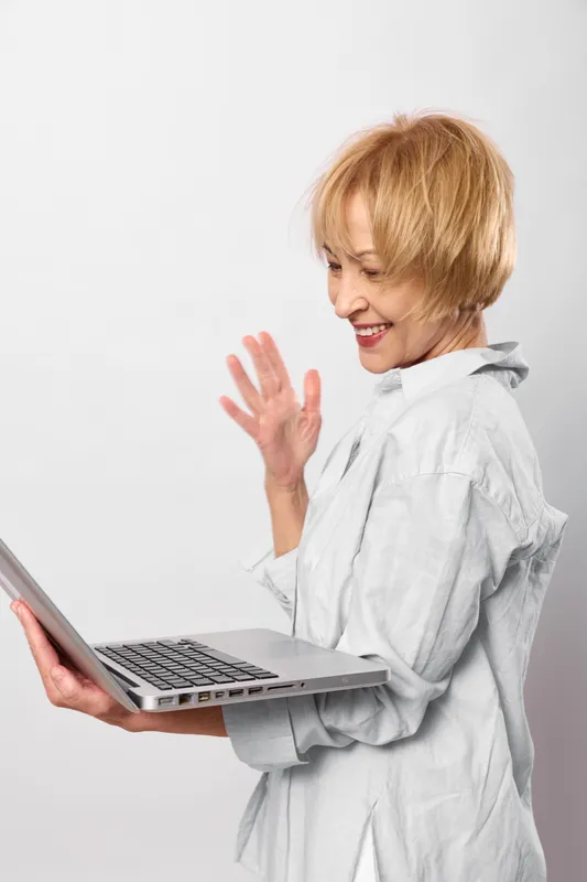 Woman with laptop smiling and waving for greeting, communication with technology, casual indoor studio on white background, soft light, calm cheerful mood