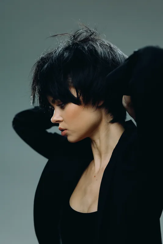Young woman with short dark hair posing with eyes closed against gray background, showing calmness and introspection mood.