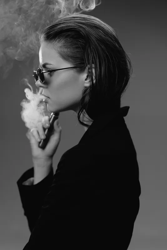 Black and white portrait of a woman vaping with sunglasses and confident expression, stylish and modern.