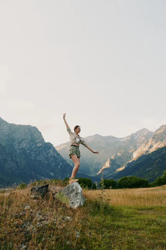 Young woman with short hair balances on a rock in a mountain meadow enjoying nature and freedom during a sunny day outdoors.