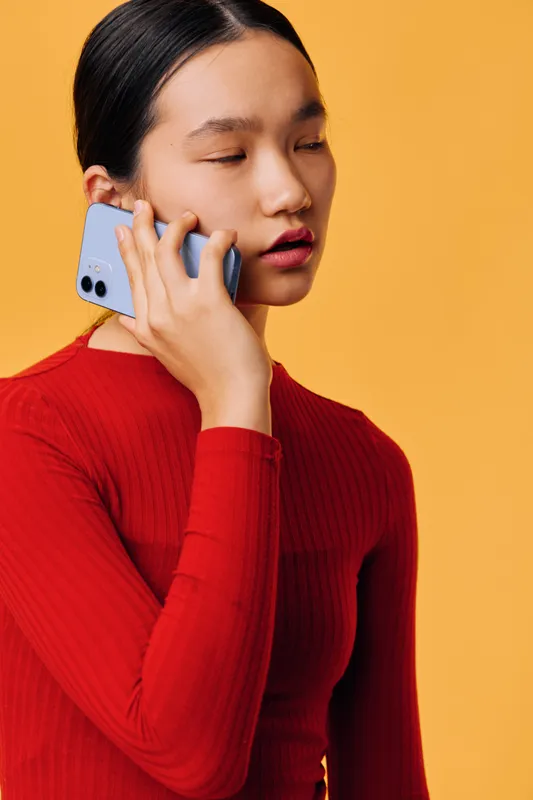 Young woman in red sweater using smartphone for a call, portrait on yellow background with closed eyes, communication, technology, connection in casual outfit and modern style.