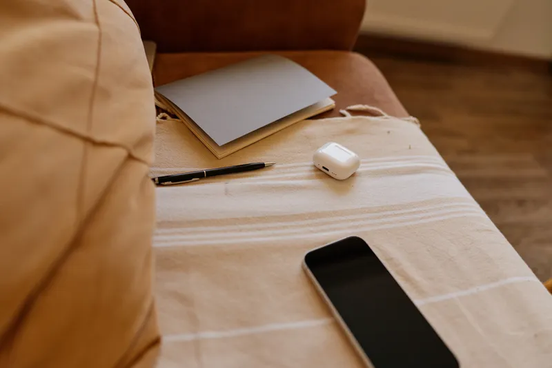 Casual home workspace on a bed with notebook, pencil, phone and earbuds, conveying a calm, organized lifestyle moment in a cozy living space, highlighting everyday planning and personal productivity
