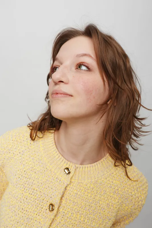 Young woman with natural skin and freckles looks sideways wearing a yellow knitted sweater. Studio portrait on white background with soft lighting and casual style concept.