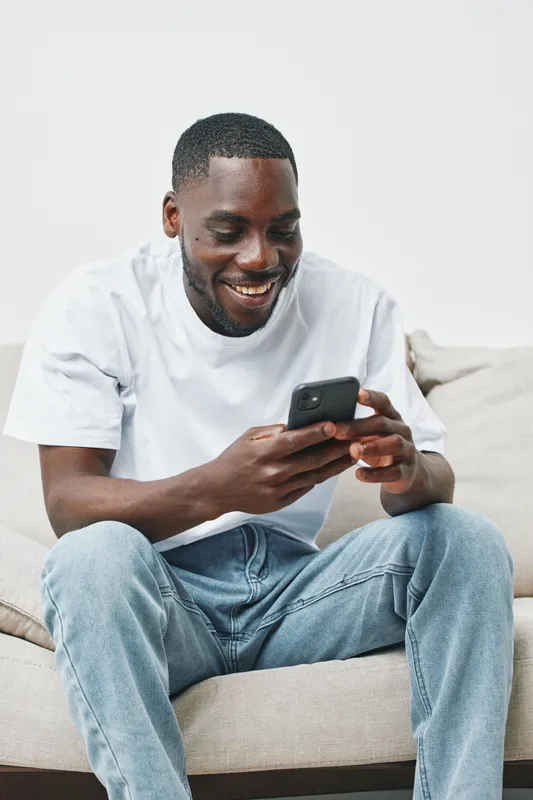 Smiling young man using smartphone at home, wearing casual white t shirt and jeans, creating a relaxed atmosphere, perfect for social media engagement
