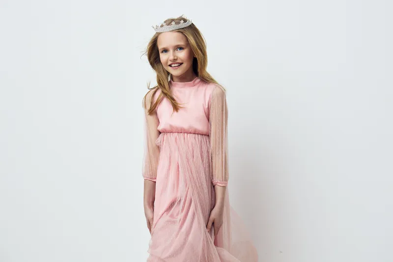 Cheerful young girl in a pink dress with long sleeves and a tiara, perfect for celebrations or fashion themed projects