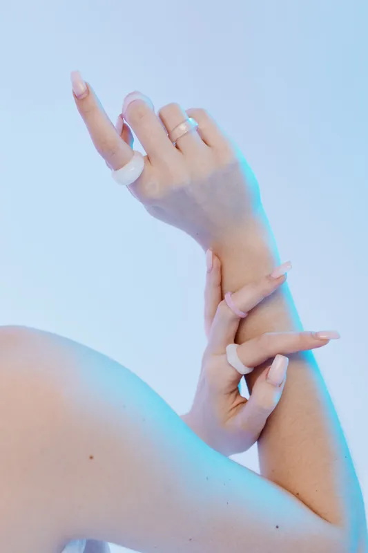 Close-up of a woman beauty fashion hands with nude manicure and modern rings on a light blue background. Concept for elegance, style, and minimalistic jewelry.