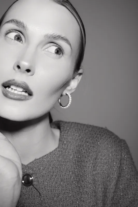 Closeup of a young Caucasian woman with fair skin looking sideways wearing hoop earrings and textured sweater. Black and white portrait with soft lighting.
