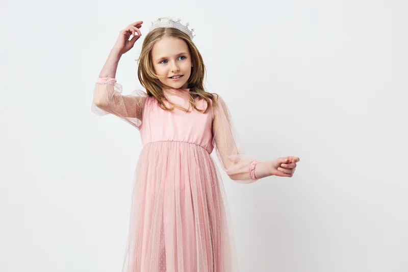 Sweet little girl in a pink tulle dress, wearing a delicate crown, expressing joy against a minimalistic white background, perfect for children s fashion concepts