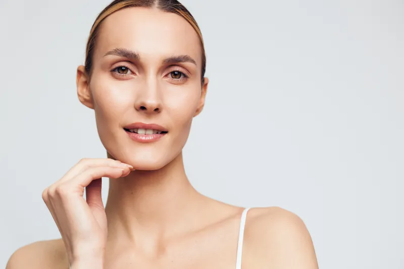 Young woman with clear skin in a close up portrait against a light background, the soft lighting highlights a calm, natural beauty mood and simple elegance.