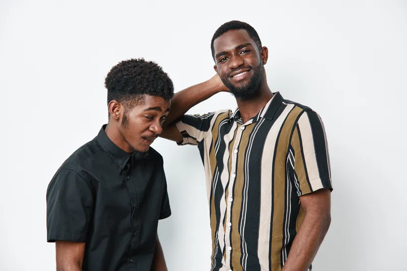 Two African American men with dark skin posing together on white background, casual clothing, smiling and relaxed, friendship and diversity concept in studio portrait.
